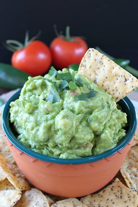 A small bowl with guacamole in it and a tortilla chip placed in the dip.