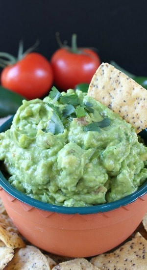 A small orange bowl with green trim filled with homemade fresh spicy guacamole.