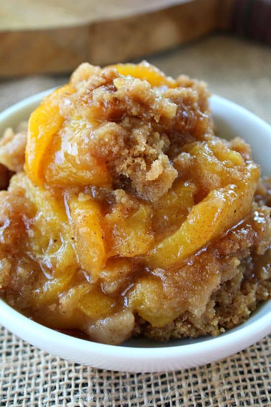 A small white bowl with a serving of peach crisp.