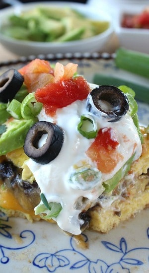 A close up of a serving of an omelette with sour cream, black olives, avocado and black beans on it.