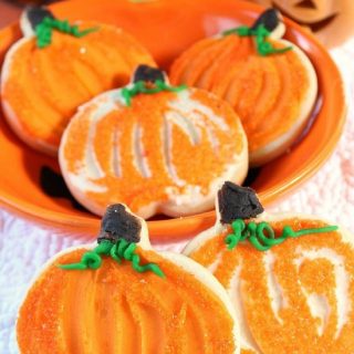 A white surface with pumpkin shaped cookies with orange frosting on them.