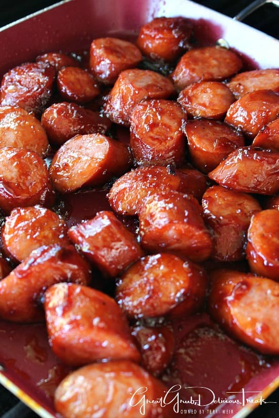 A grill pan with grilled pieces of smoked sausages covered in barbecue sauce.