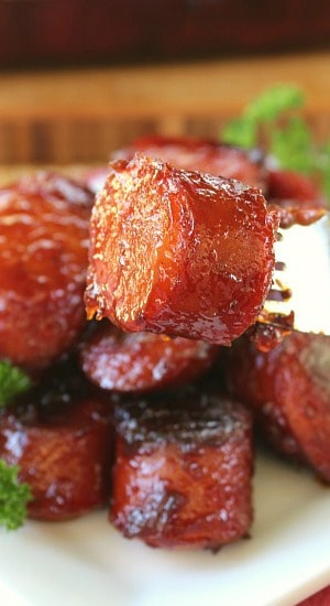 A close up photo of a few bites of barbecue smoked sausages on a white plate.