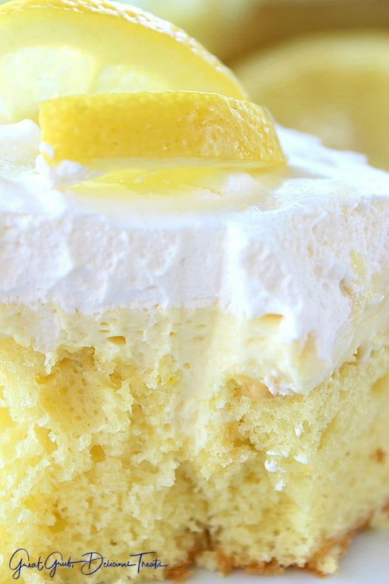 A close up of lemon poke cake with cool whip topping and lemon slices.