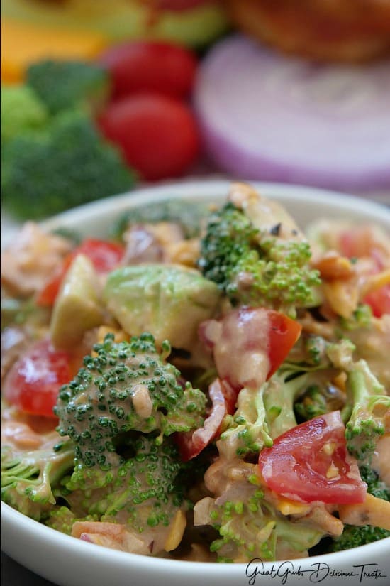 A close up of broccoli salad with tomatoes, avocados, bacon, cheese in a creamy sauce.