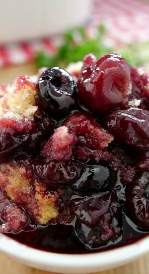 A close up of a white bowl filled with cherry cobbler.