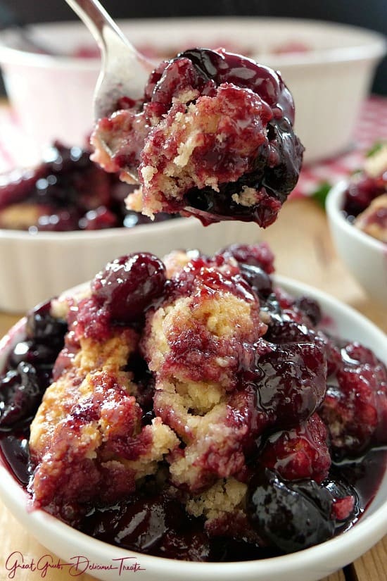 A spoonful of cherry cobbler being held a bowl full of cobbler.