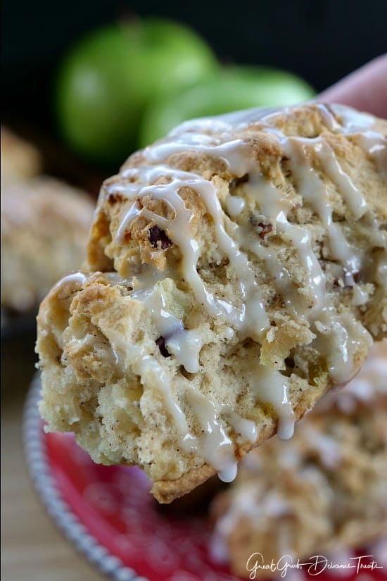 Apple Pecan Scone being held up showing the glaze drizzled over the top with green apples in the background.