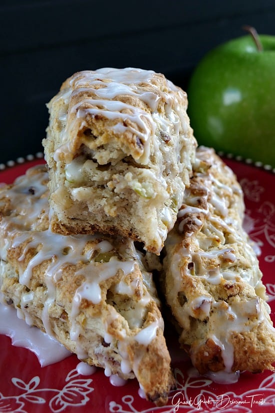 Three apple pecan scones sitting on a red plate with a green apple in the background.