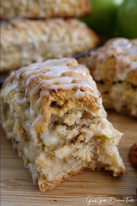 A photo of an apple pecan scone with a bite taken out, sitting on a cutting board with other scones in the background.