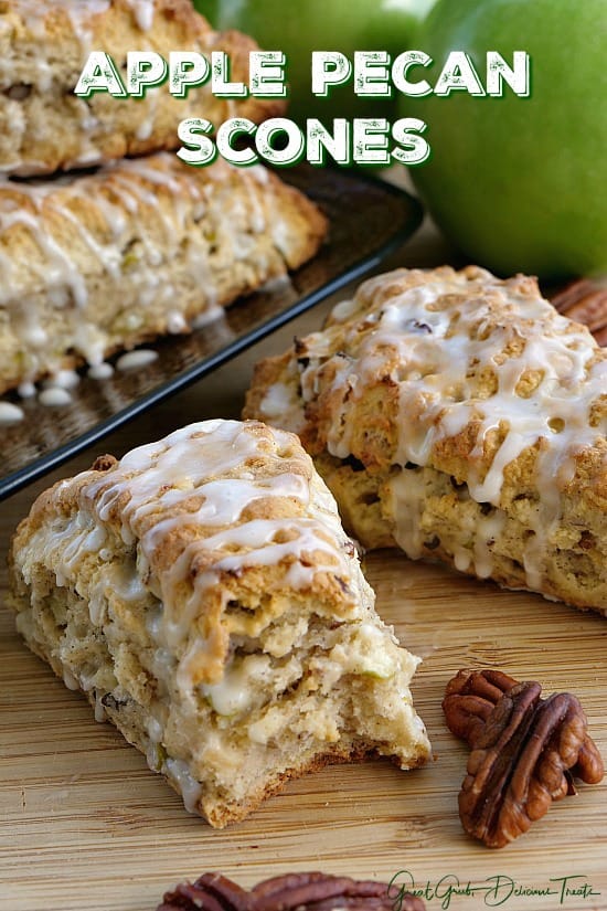 Apple Pecan Scones - 4 scones with glaze drizzled over the top, one with a bite taken out with pecans and apples in the background.