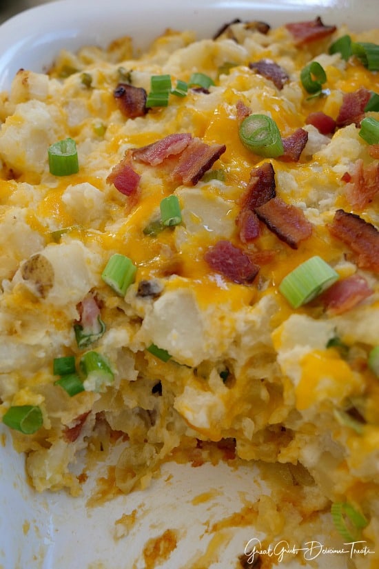 Loaded Baked Potato Casserole - a white casserole dish filled with loaded baked potato casserole topped with green onions, bacon and more cheese.