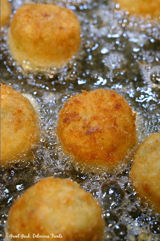 A close up of  bite-size appetizer being fried in a pan with the oil bubbly.