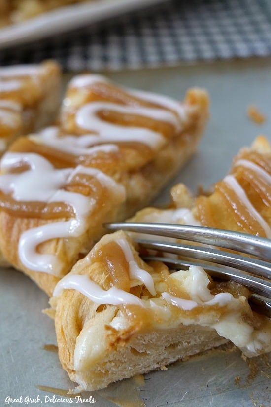 Cream Cheese Caramel Apple Crescent Ring - photo of 3 triangle shaped crescents filling with apples and cream cheese with caramel and glaze drizzled over the top and a fork taking a piece from one.