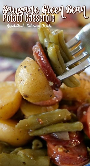 A fork with a bite of potato, green beans and a slice of kielbasa on it.