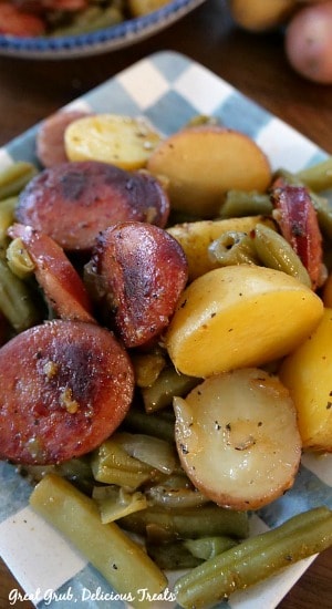 A light blue and white checkered plate with a serving of potatoes, green beans and sausage on it.