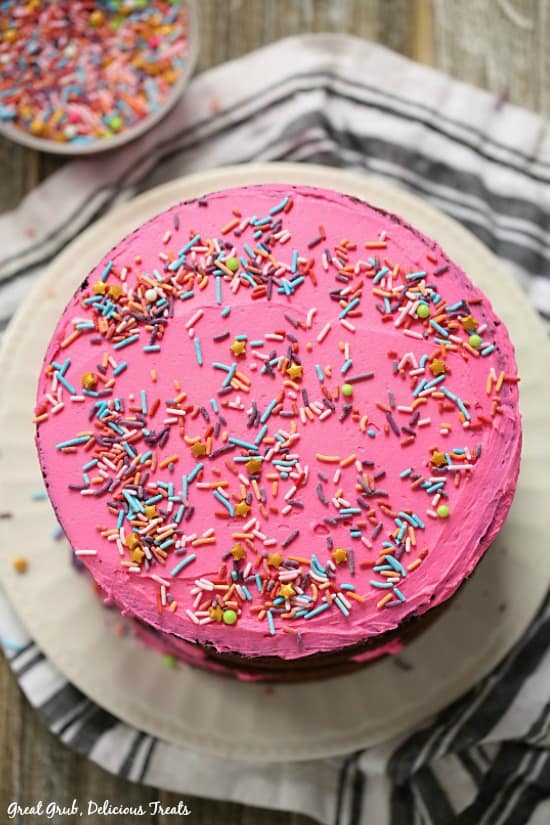 Chocolate Triple Layer Cake topped with pink buttercream frosting and candied sprinkles