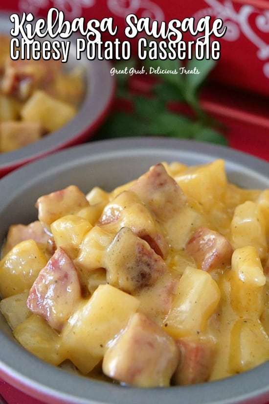 A red and silver bowl filled with a serving of cheesy potatoes and kielbasa.
