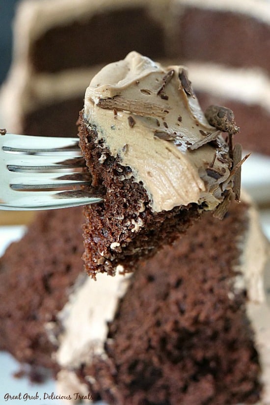 A bite of chocolate cake on a fork with the frosting and chocolate shavings on it.