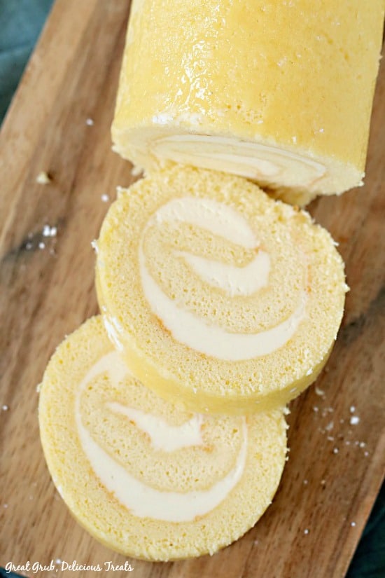 Lemon Cake Roll is placed on a wooden cutting board with two slices of cake laying nicely on the cutting board.