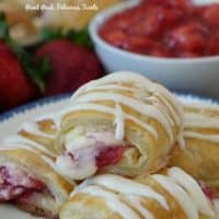 Strawberry cream cheese filled pastry strudels stacked on a plate drizzled with icing.