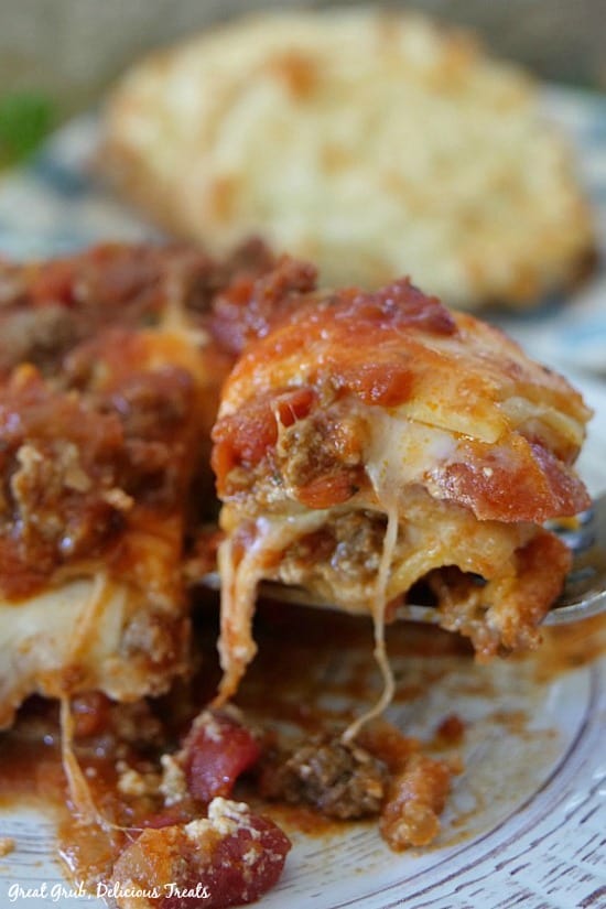 Best Homemade Lasagna is a piece of lasagna with a fork full of lasagna with a piece of garlic bread in the background.