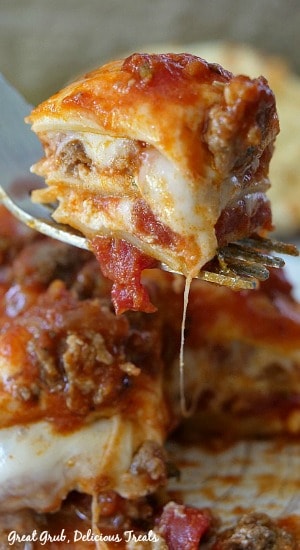 A bite of lasagna on a fork with a slice in the background.
