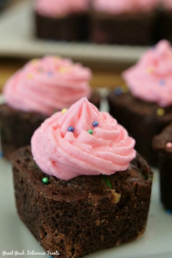 Chewy Brownie Bites are bite size brownies with pink frosting sitting on a white plate.