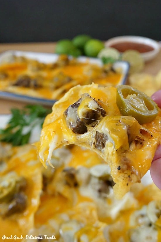 Rib Eye Nachos - A picture of someone holding a tortilla chip with melted cheese, meat and a sliced jalapeno.
