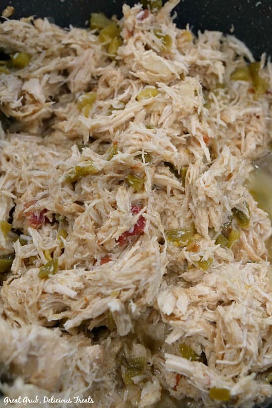 Crock Pot Spicy Chicken - shredded chicken in the crock pot that shows the shredded chicken, diced jalapenos and tomatoes.