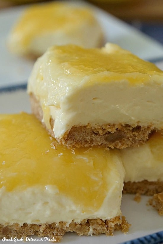 Lemonade Cheesecake Bars - 3 cheesecake bars, two on a white plate with one bar sitting on top and one cheesecake bar in the background.