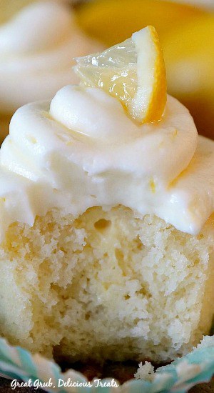 A close up photo of a lemon cupcake with a bite taken out and a small lemon wedge on top.