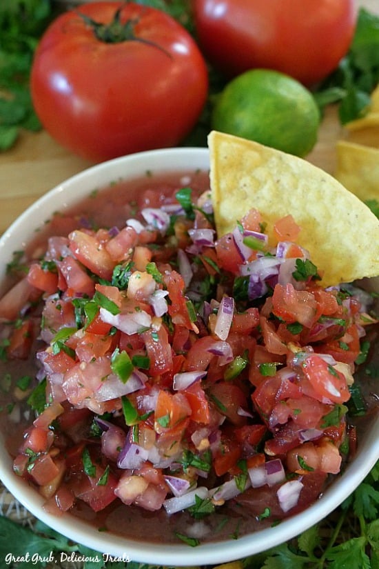 Pico de Gallo - a white bowl filled with chopped tomatoes, onions, cilantro, peppers with a chip placed in the bowl.
