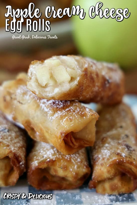 Apple Cream Cheese Egg Rolls - a white and blue checkered plate with 5 egg rolls positioned on top of each other with one showing the apple cream cheese filling inside.