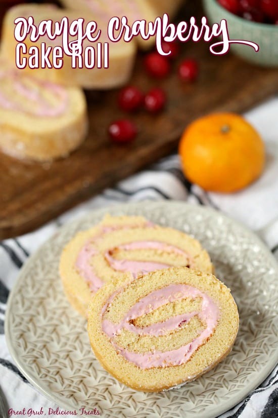 Orange Cranberry Cake Roll - Slices of cake sitting on a grey plate and brown cutting board with an orange and loose cranberries in the background.