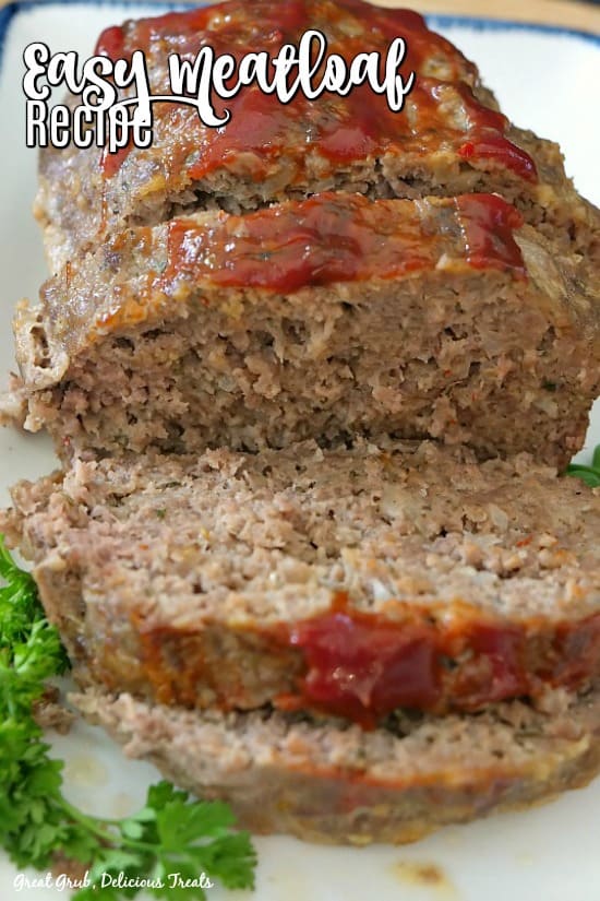 Easy Meatloaf Recipe - a loaf of meatloaf with a few slices made in the meatloaf on a white plate with blue trim, garnished with parsley.