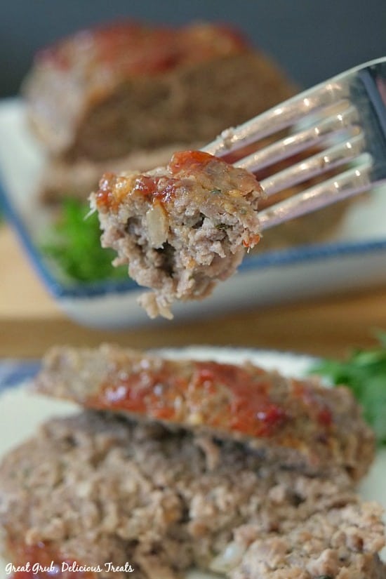 Easy Meatloaf Recipe - a photo of a bite of meatloaf on a fork with the meatloaf in the background and another plate with two slices of meatloaf on it.