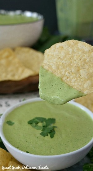 A white bowl filled with creamy jalapeno cilantro salsa with a chip having been dipped in the salsa.