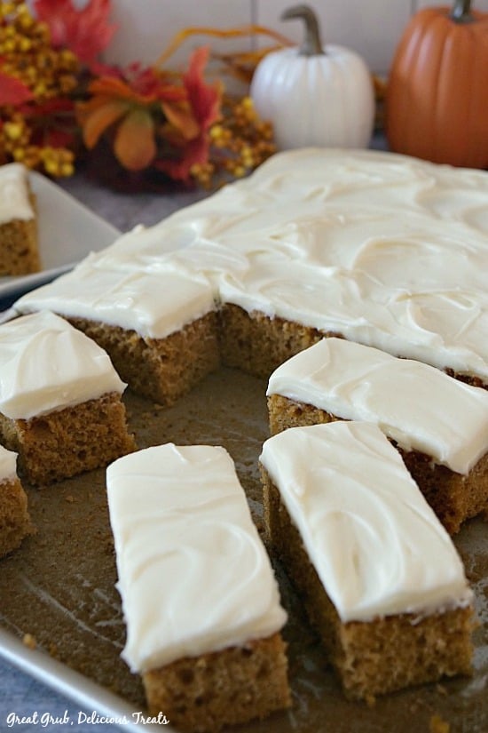 Pumpkin Bars with Cream Cheese Frosting - a sheet pan with frosted pumpkin bars sitting on it with two pumpkins and fall flowers in the background.