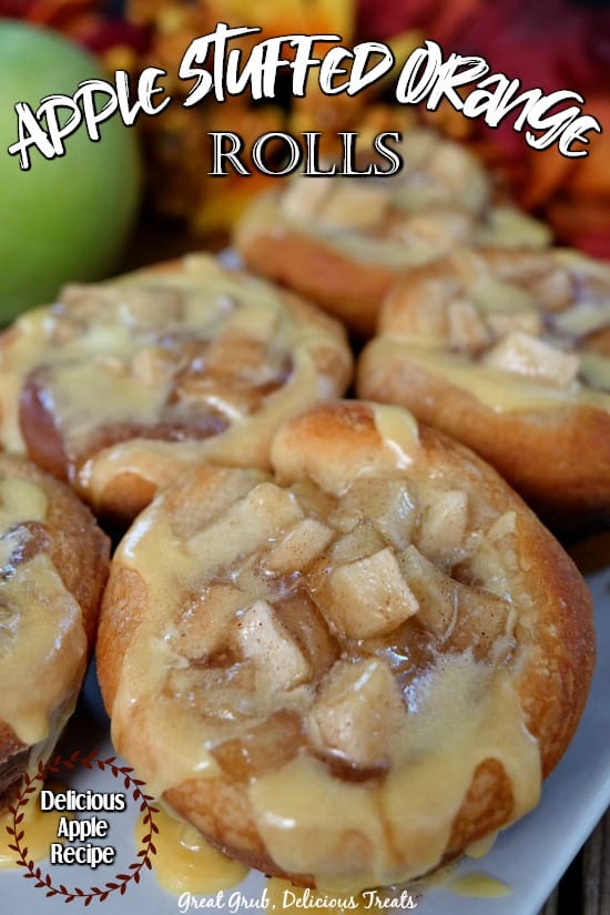 Apple Stuffed Orange Rolls - 5 cinnamon rolls stuffed full with an apple filling, all sitting on a white plate with a green apple and fall foliage in the background.