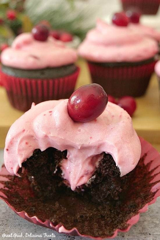 A picture of a chocolate cupcake with a bite taken out showing the cranberry filling and frosting with a cranberry on top.