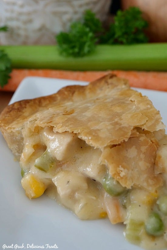 A slice of chicken pot pie on a white plate with celery and parsley in the background.
