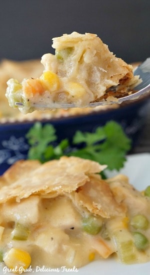 A piece of chicken pot pie on a fork with a slice of pot pie on a white plate garnished with parsley with a blue pie pan in the background 