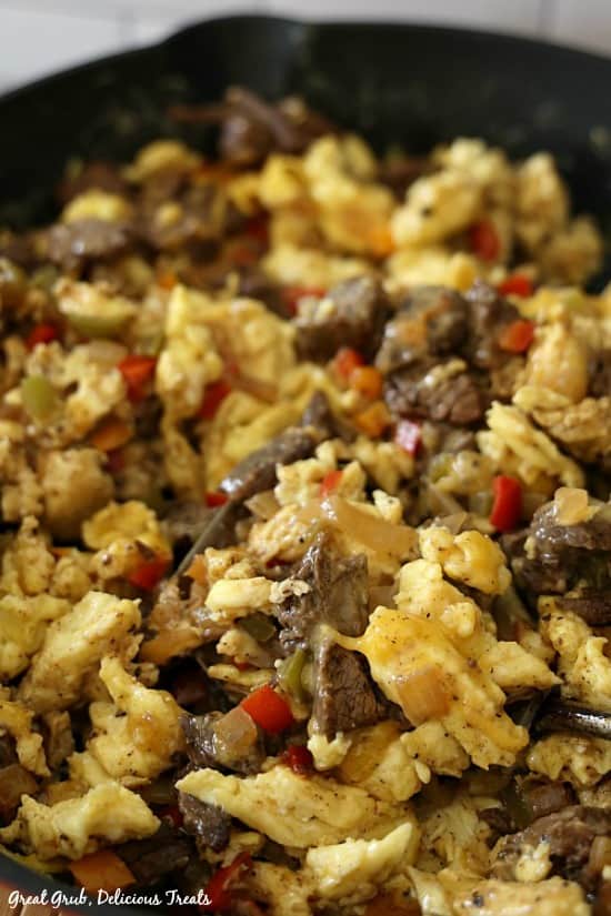 Beef Fajita Breakfast Scramble is shown in a skillet showing all the ingredients: beef fajita meat, scrambled eggs, diced up bell peppers, onions and melted cheese.