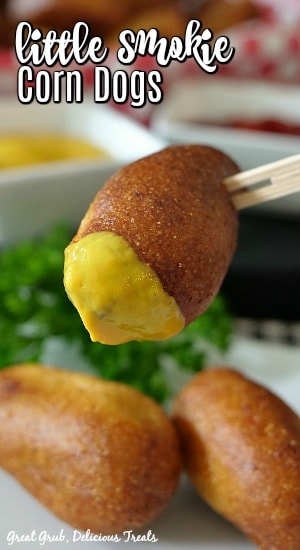 Mini corn dogs on a white plate with one corn dog dipped in mustard.