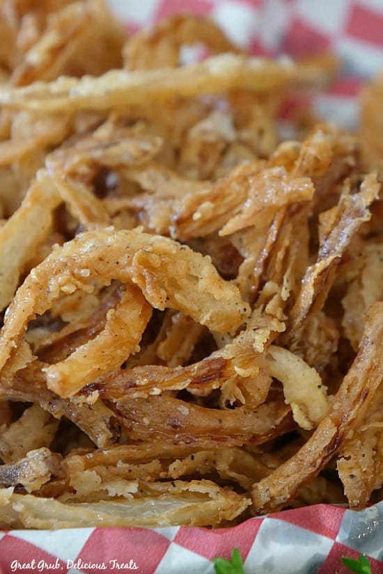 A close up picture of fried onion strings on a red and white checked paper in a basket.