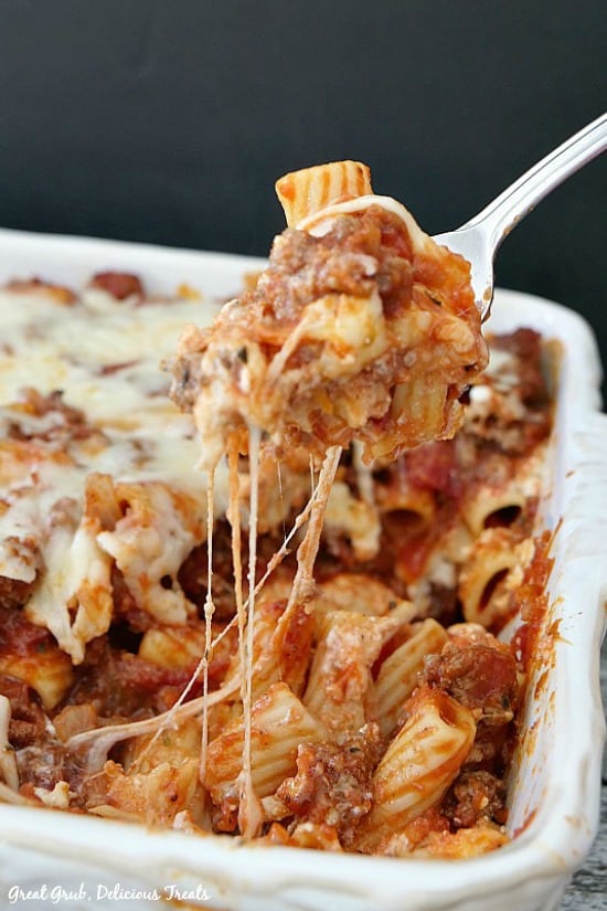 Cheesy Rigatoni Pasta Bake in a white casserole dish with a fork pulling out a bite of the pasta with the gooey cheese stringing from pasta bake to fork.