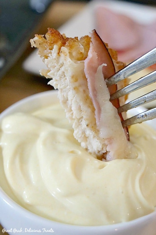 A bite size piece of Malibu Chicken on a fork being dipped into a mayonnaise/mustard dipping sauce.