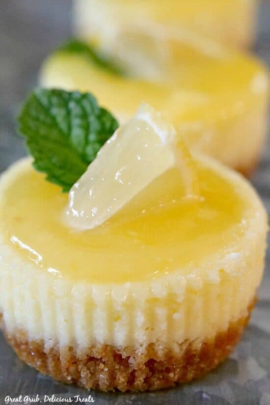 Close up photo of a mini lemon cheesecake with a small lemon wedge and a piece of mint on top.