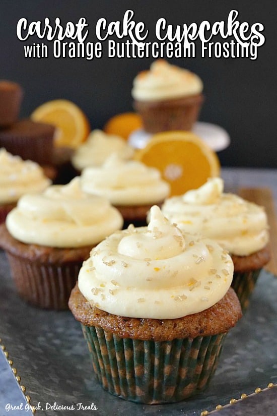 Carrot Cake Cupcakes with Orange Buttercream Frosting with orange slices in the background.